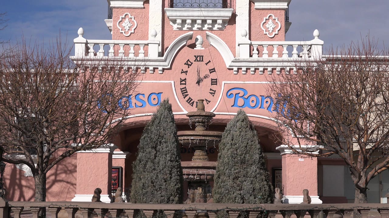 Pink building facade with clock detail, trees, and blue sky.