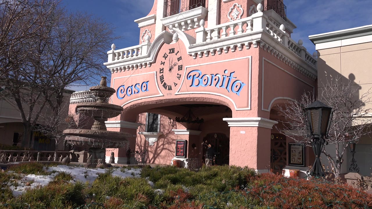 Wide Denver exterior frame of the pink Casa Bonita castle-style facade, with a tiered fountain at left, bare trees, snow patches, and small people near the arched entrance.