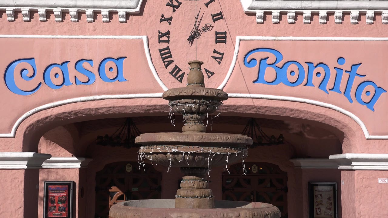 Close view of a pink facade with Casa Bonita lettering and a fountain.
