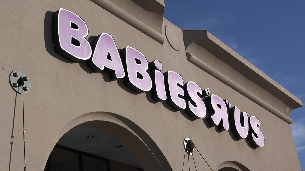 Close view of a Babies R Us sign on a beige storefront facade.