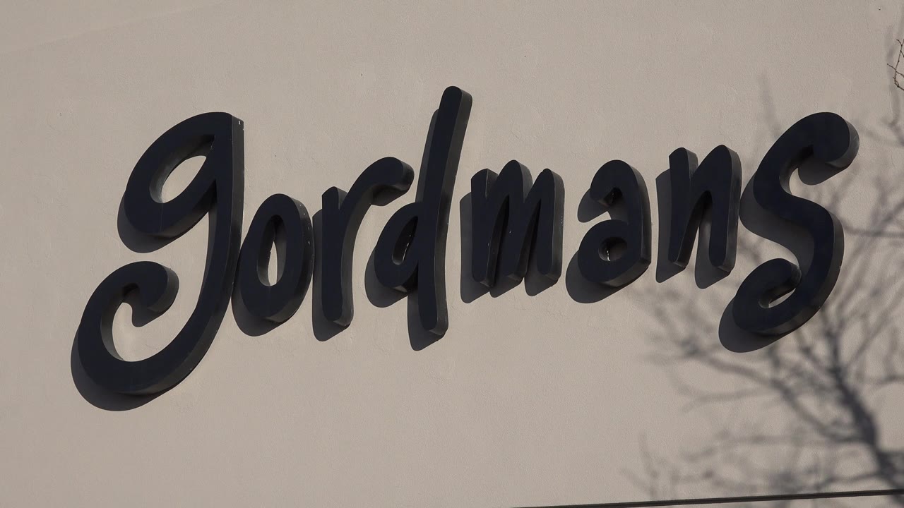 Close Denver 2015 view of the Gordmans lettering on the beige facade, with more of the right-side tree branches visible and no visible people.