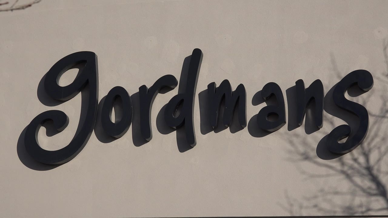 Close Denver storefront view of black Jordmans letters on a pale stucco wall, with bare branch shadows across the facade and no visible people.