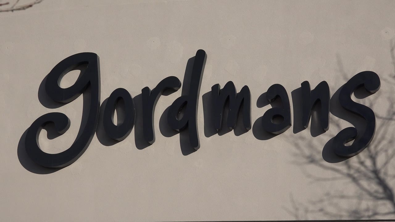 Second frame keeps the Denver retail sign large in frame, with the black letters casting shadows on the pale wall and no visible people.