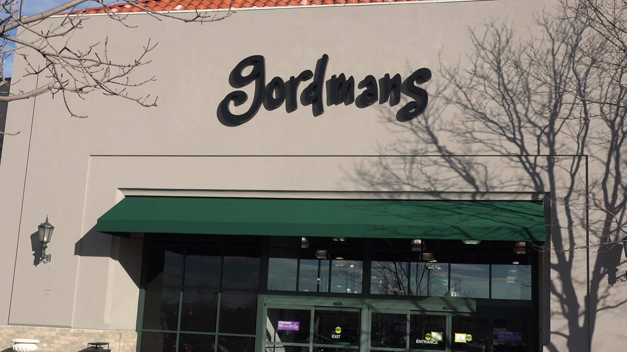 Denver, Colorado frame at 0:01 with the Gordmans logo high on the beige wall, dark glass storefront below, tree shadows across the facade, and no clearly visible people.