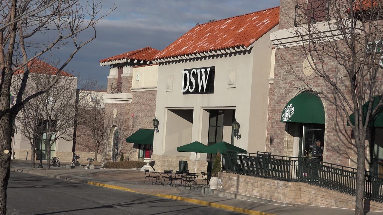 Denver shopping center exterior at the start of the clip, showing a DSW sign, a green Starbucks awning, patio furniture, leafless trees, and no visible people.