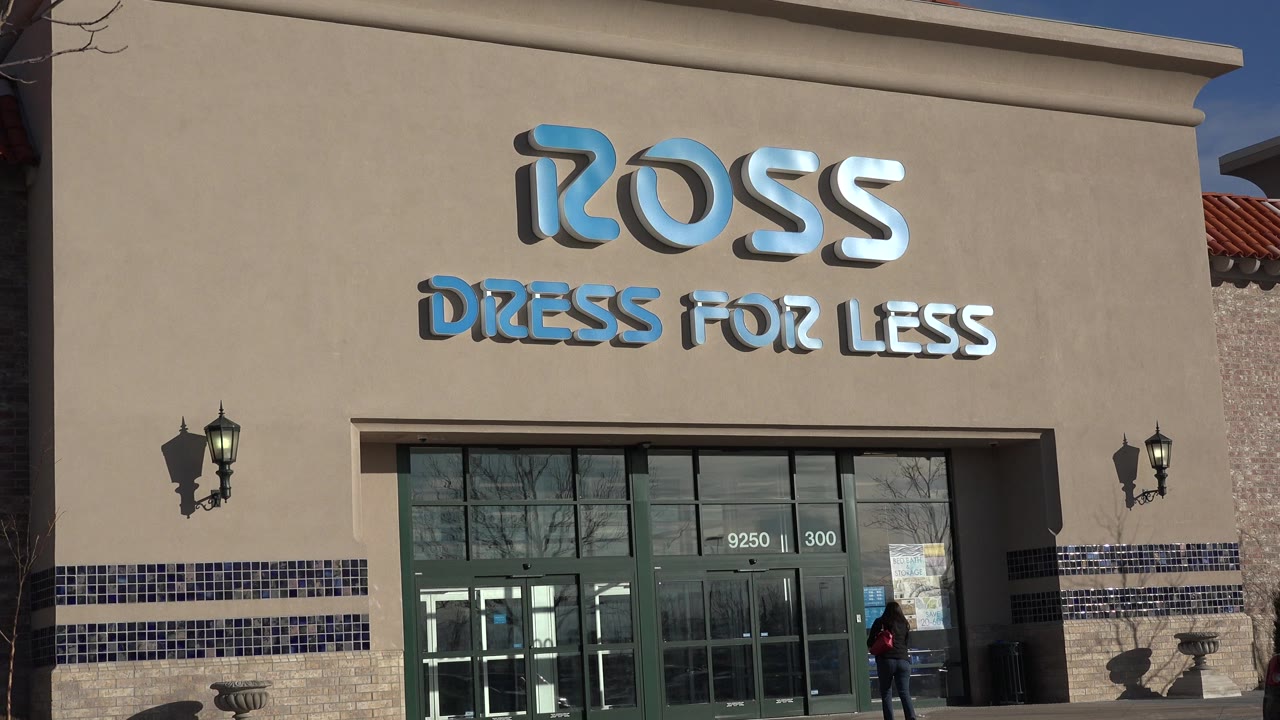 Denver, Colorado retail storefront with the Ross Dress for Less sign centered high on the tan facade, green-framed glass doors below, wall lanterns, and a small person near the right side of the entrance.