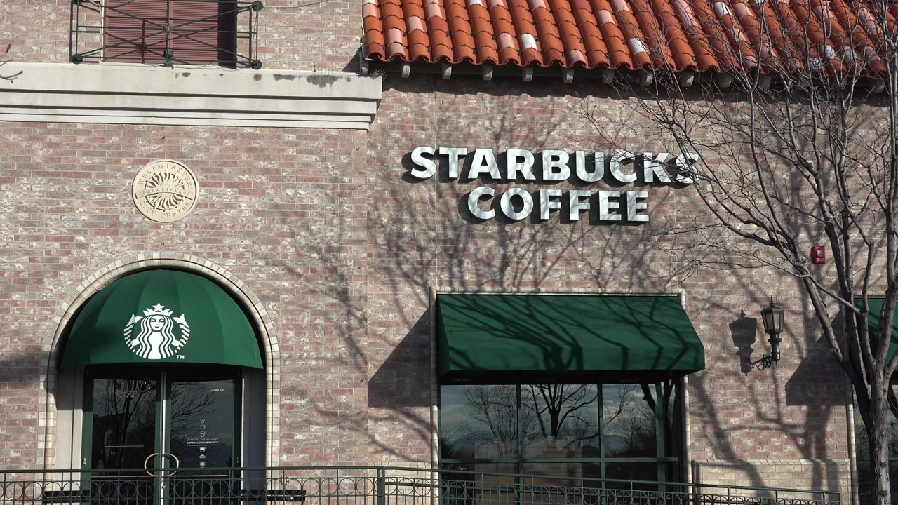 Denver coffee shop exterior with the Starbucks Coffee sign, green awnings, tree shadows across the brick, window reflections, and no visible people.