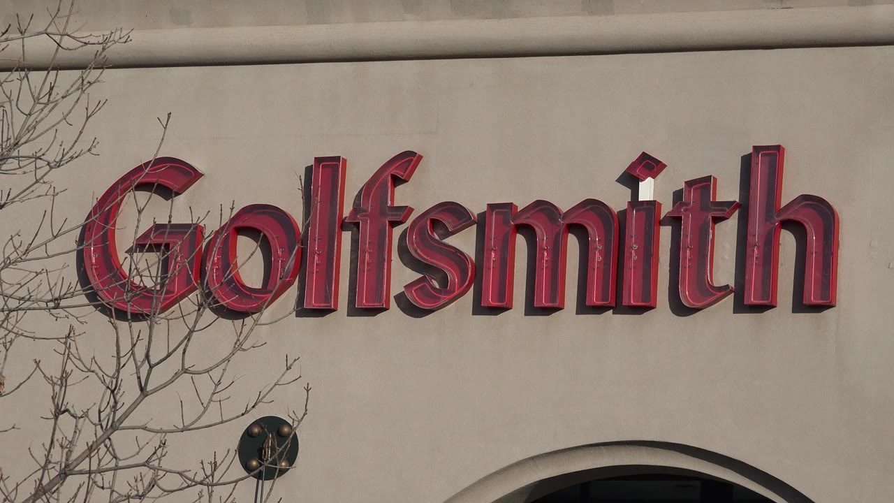 Red Goldsmith sign on a beige building facade with bare branches
