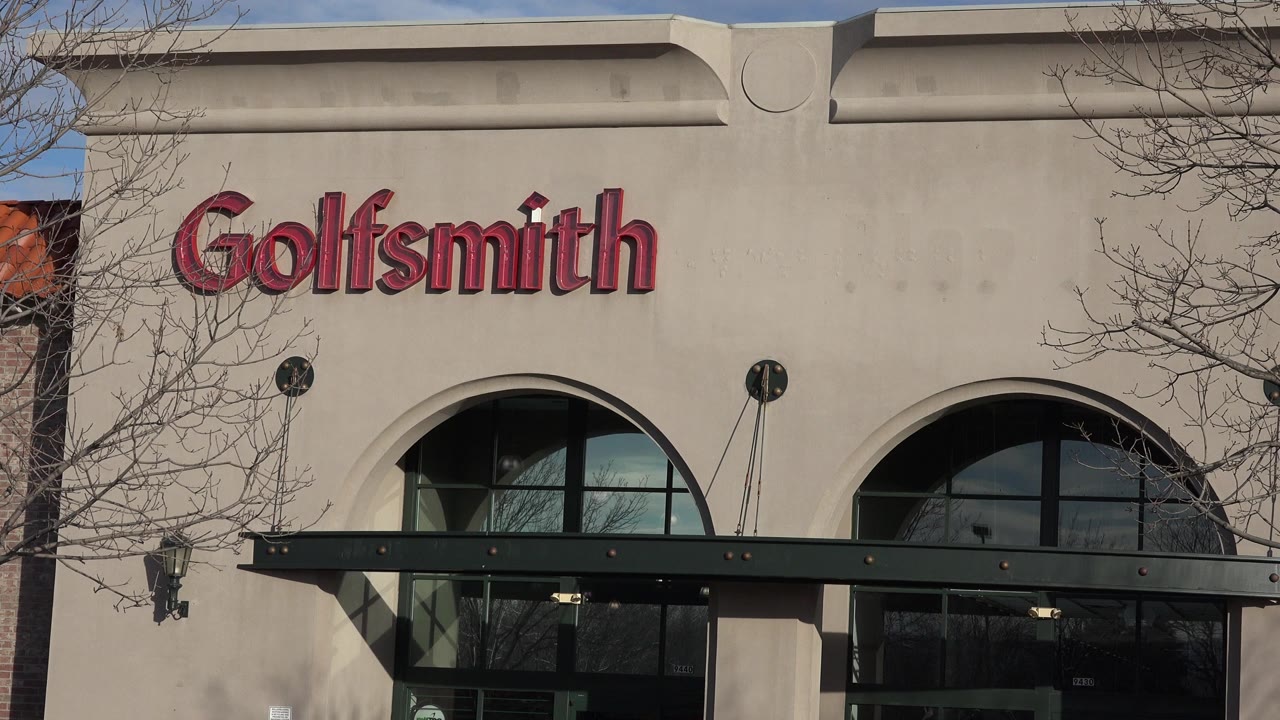 Close Denver storefront view holds on the Goldsmith sign, arched glass, black canopy hardware, bare tree branches, and no visible people.