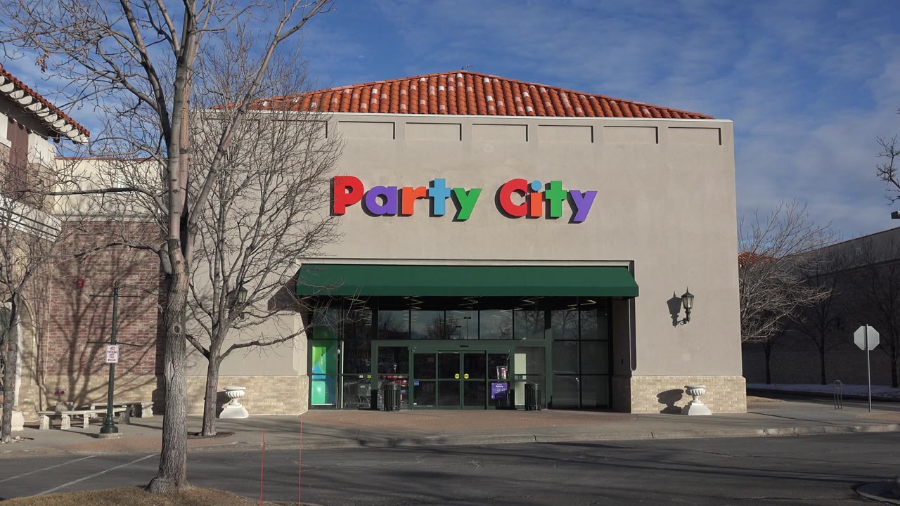 Denver retail exterior centered on the Party City sign and glass doors, with leafless trees crossing the facade and no visible people.