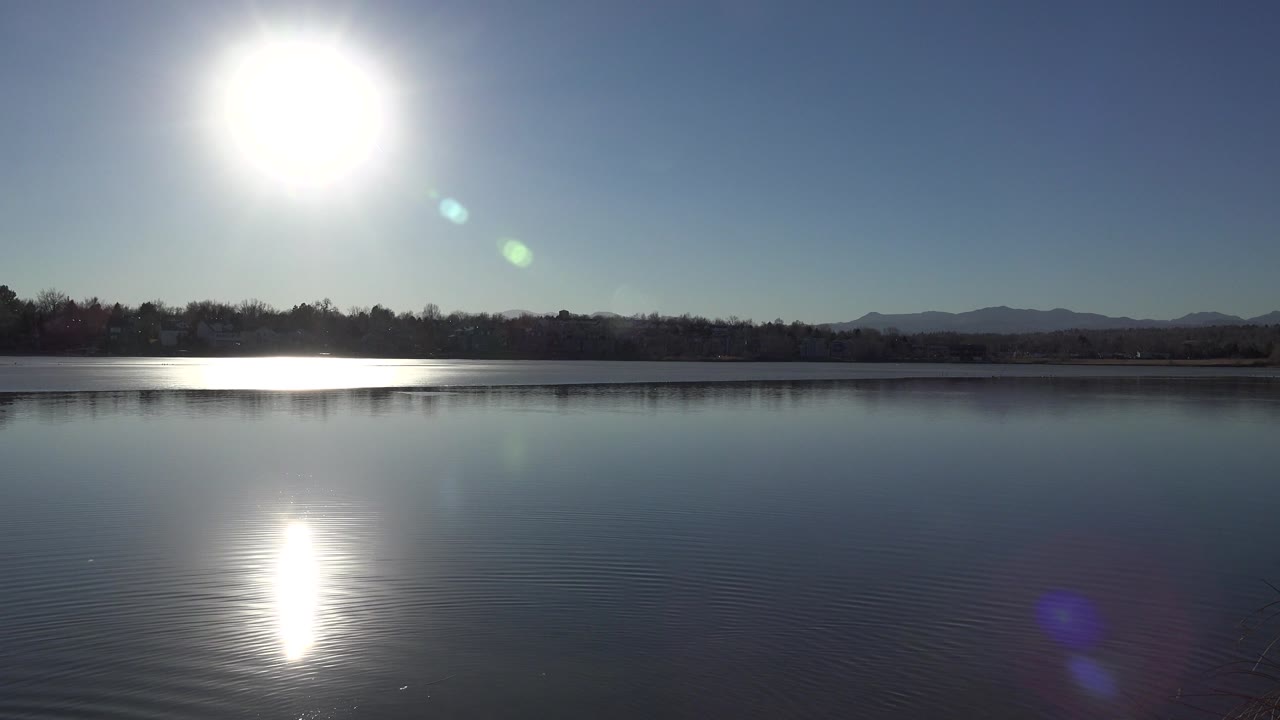 Bright sun over a lake with glare on rippled water and distant hills.