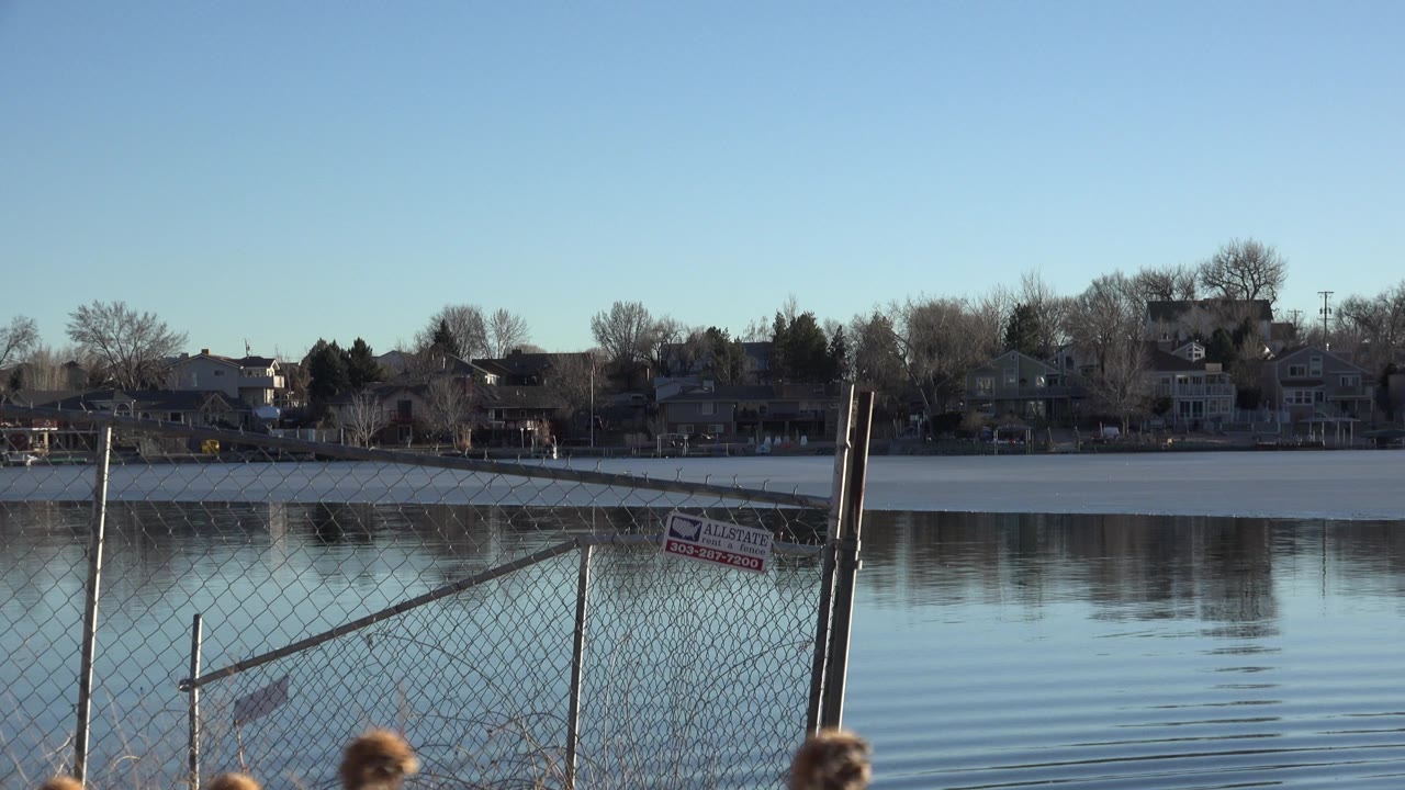 Lake behind a chain-link fence with houses across the water.