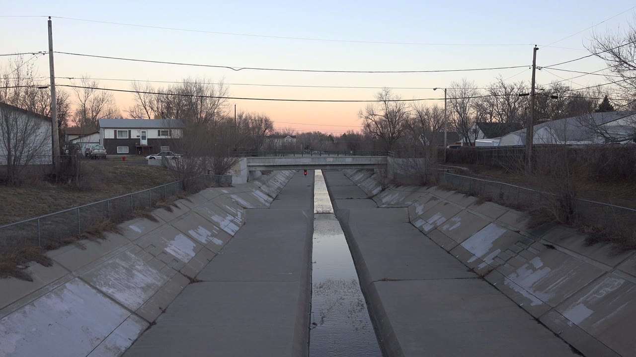 Concrete drainage channel under a road bridge at sunset.