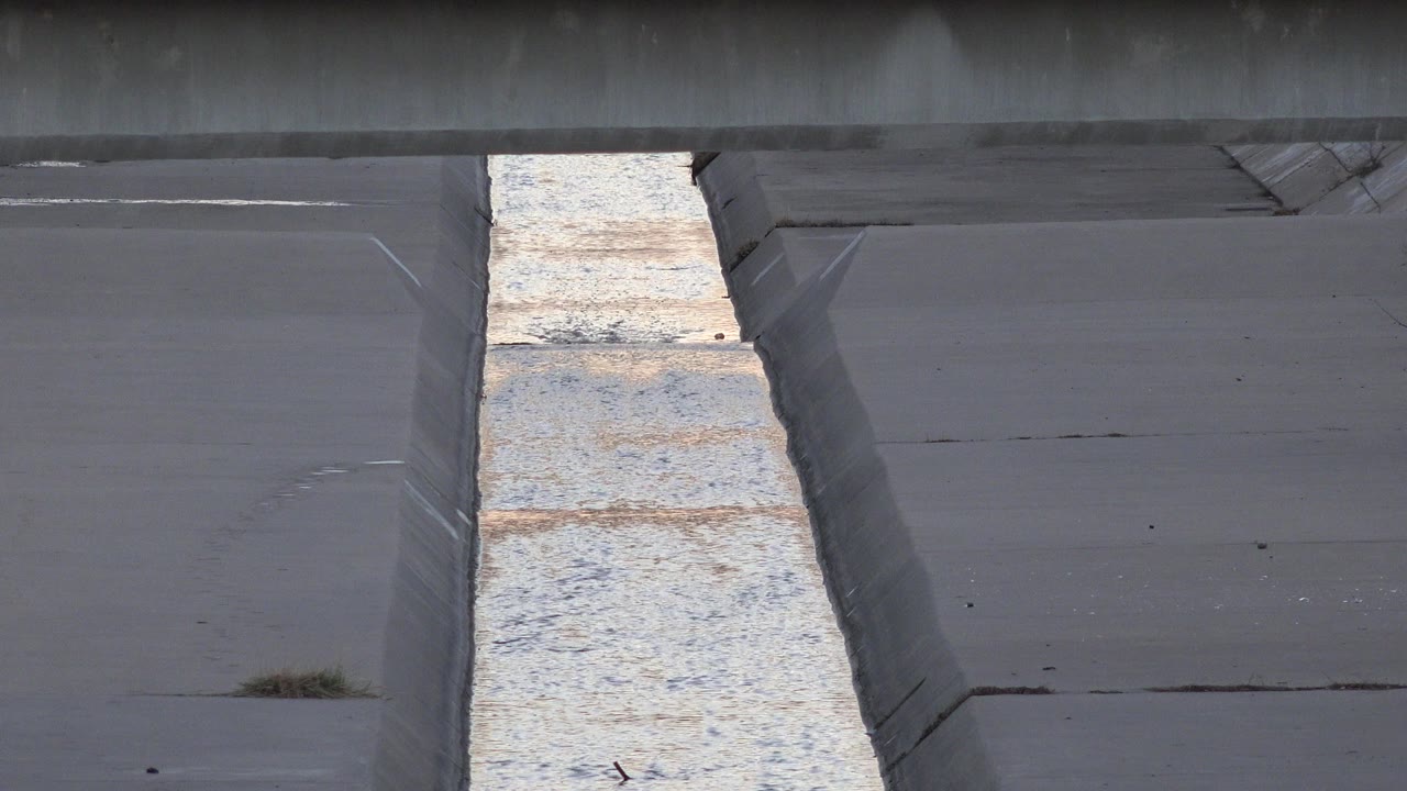 A Westminster, Colorado concrete stream channel holds a bright strip of rippling water between gray sloped banks, with no visible people.