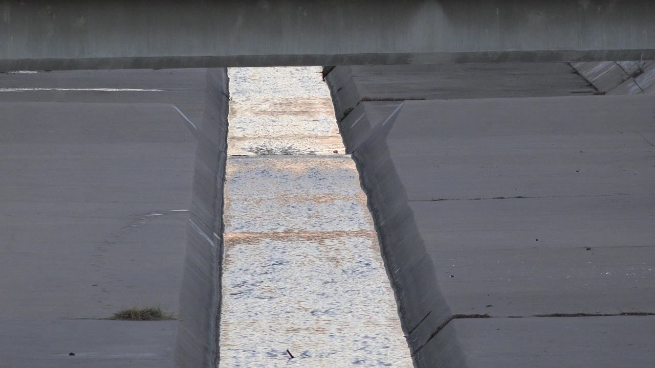 A Westminster, Colorado concrete drainage channel fills the frame, with pale water running through the center and no visible people at the start of the clip.