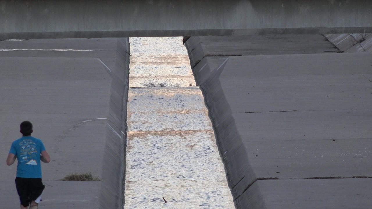 Man jogging away beside a concrete water channel.