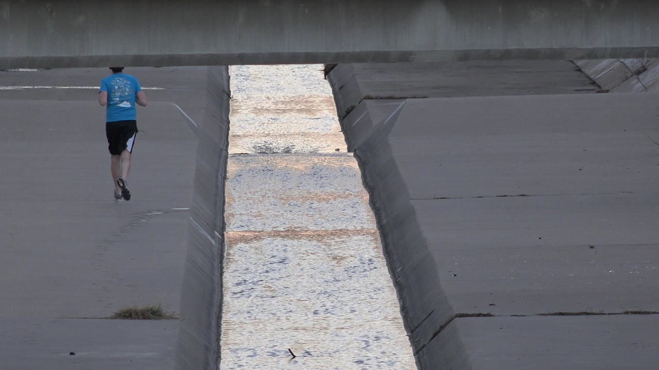 Runner near the upper frame beside the canal and bridge shadow.