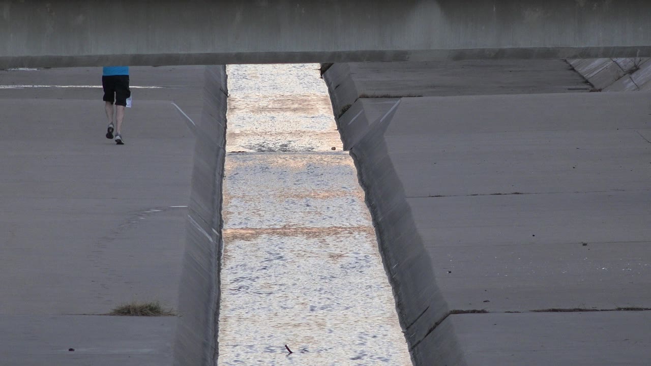 Runner small in frame above a concrete canal channel