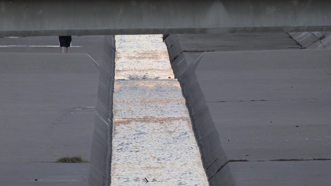 The water strip catches pale light between sloped concrete sides while the partially visible person remains near the top of the Westminster channel frame.