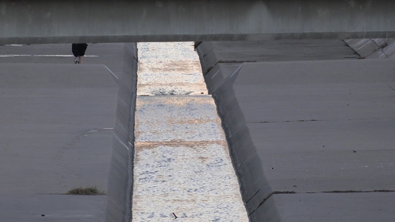 Concrete drainage channel with a small cropped figure near the top.