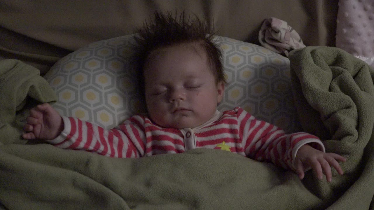 Sleeping baby under a green blanket on patterned bedding.