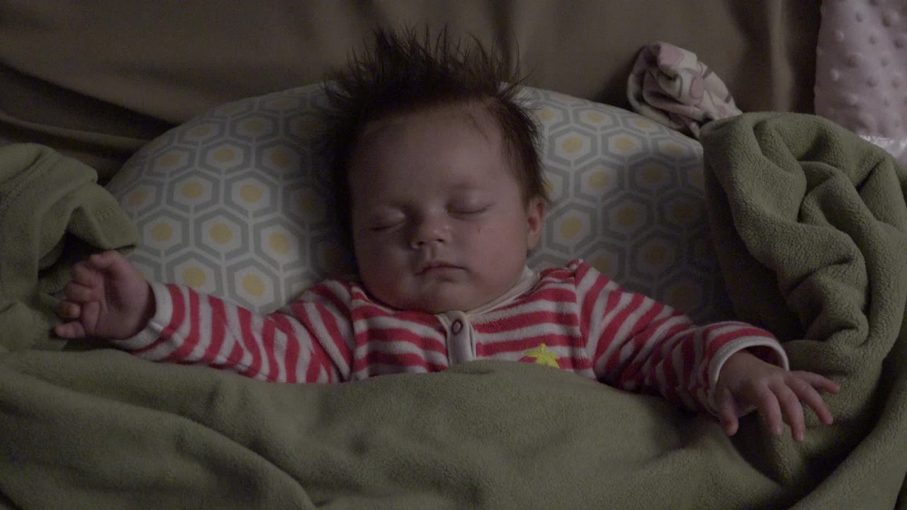 The baby remains asleep in Westminster, Colorado with eyes closed, arms relaxed, and the green blanket covering the lower body.