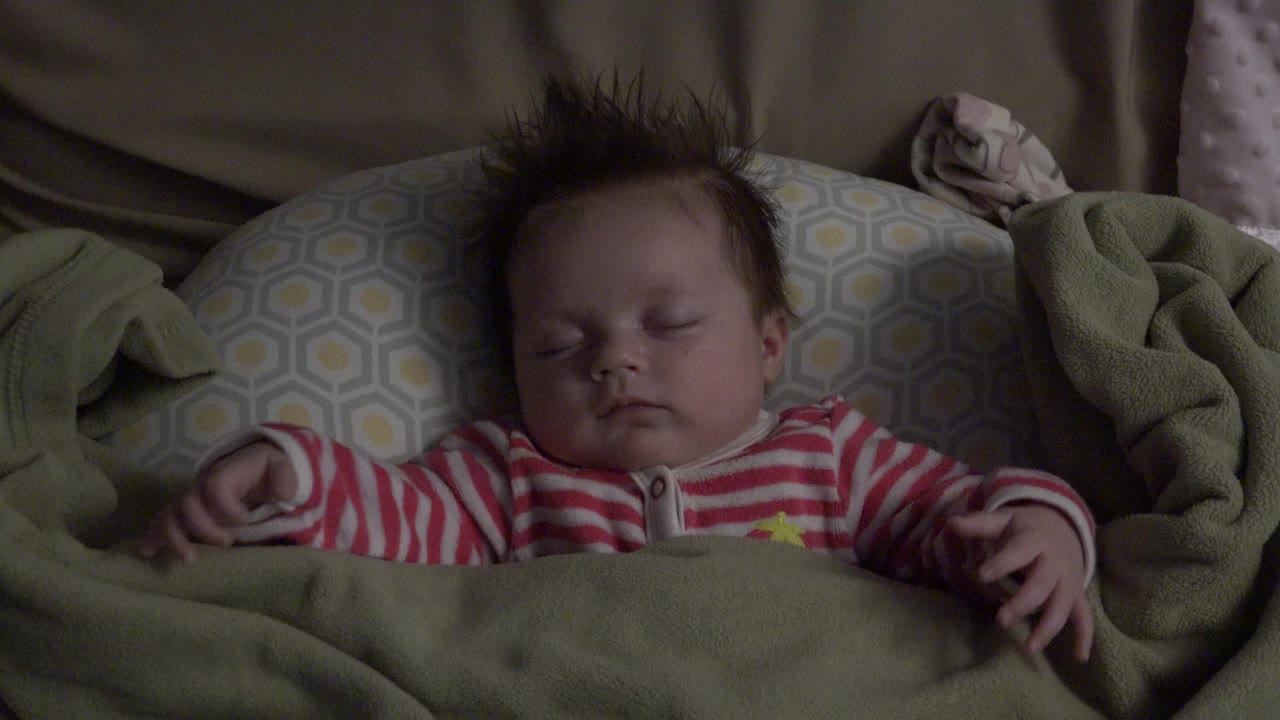 Sleeping baby in a striped outfit under a green blanket.