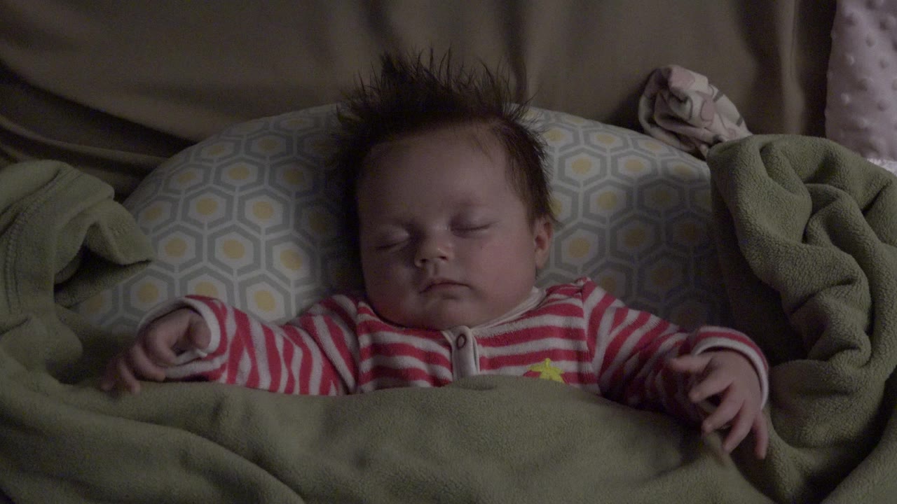 A close view shows the sleeping baby in Westminster, Colorado with the right hand lifted slightly above the green blanket.
