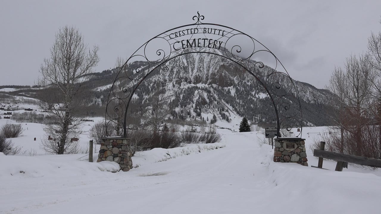 Snowy cemetery entrance arch with mountains behind it