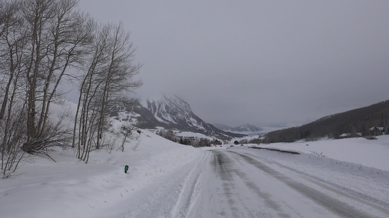 Snowy road leading toward distant mountains under a gray sky.