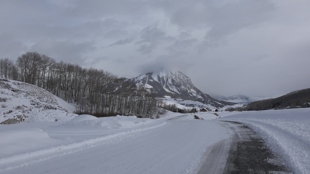 Curving snowy road with open snowfield and mountain in the background.