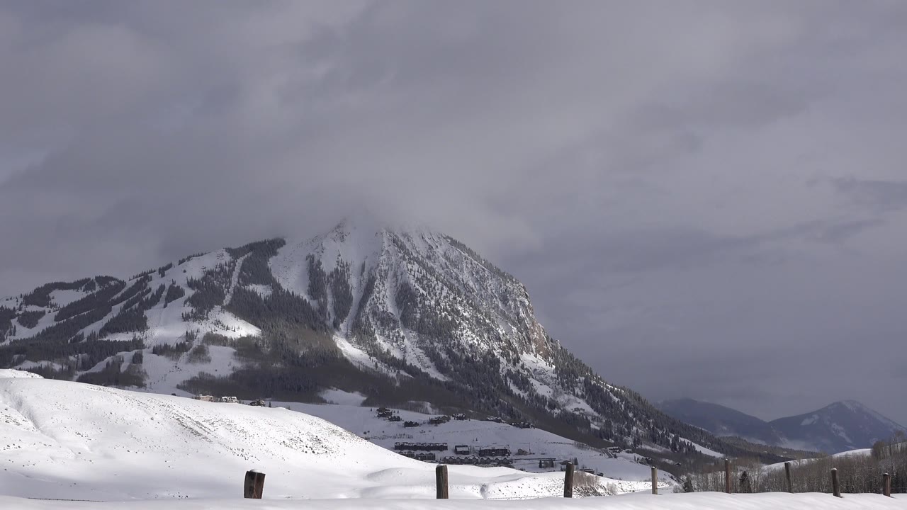 Early frame showing the Crested Butte, Colorado mountain centered above a bright snow-covered slope, with distant ridges at right and no visible people.
