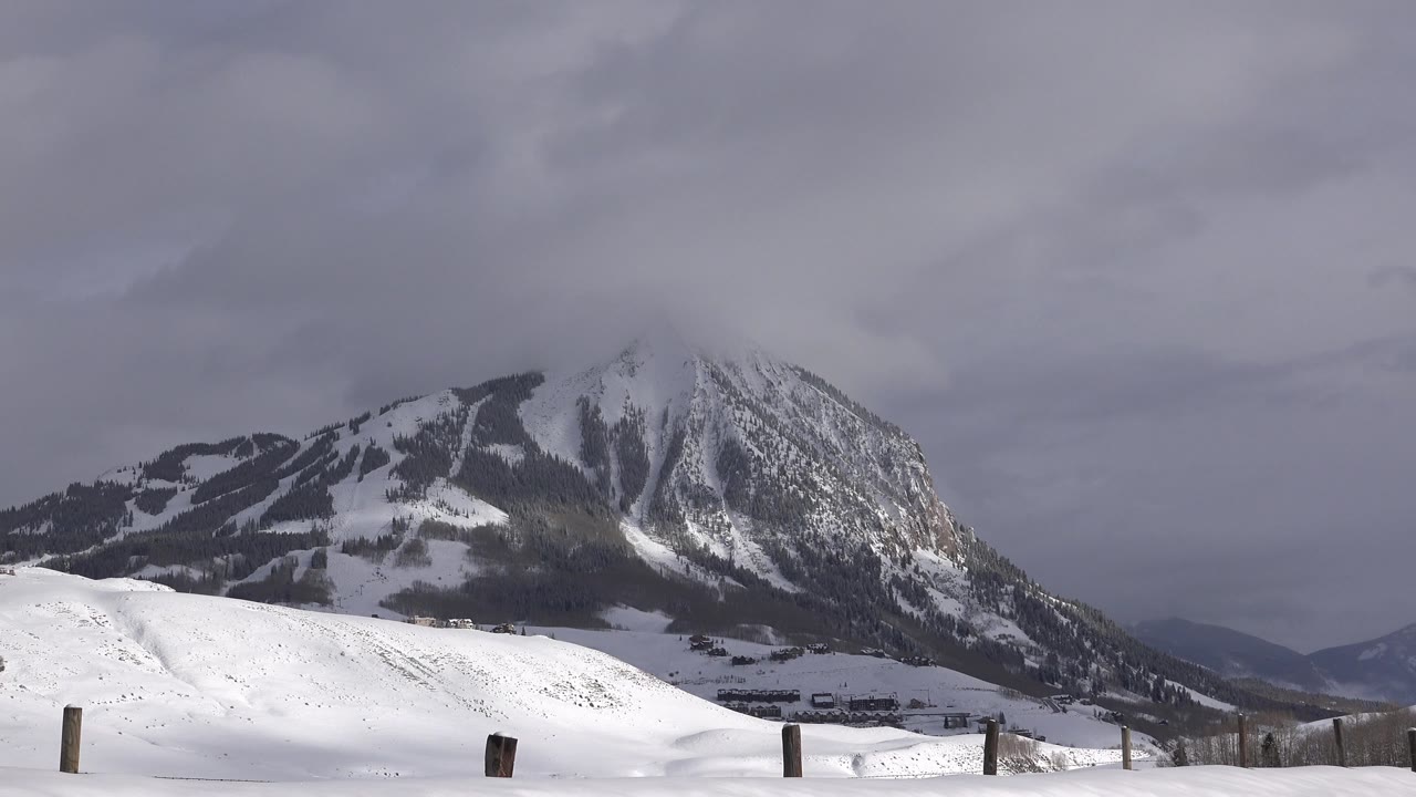 Snowy foreground ridge below a dark mountain and overcast sky