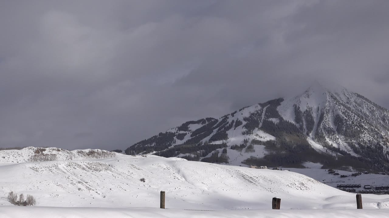 Wide snowy landscape with fence posts and a cloudy mountain