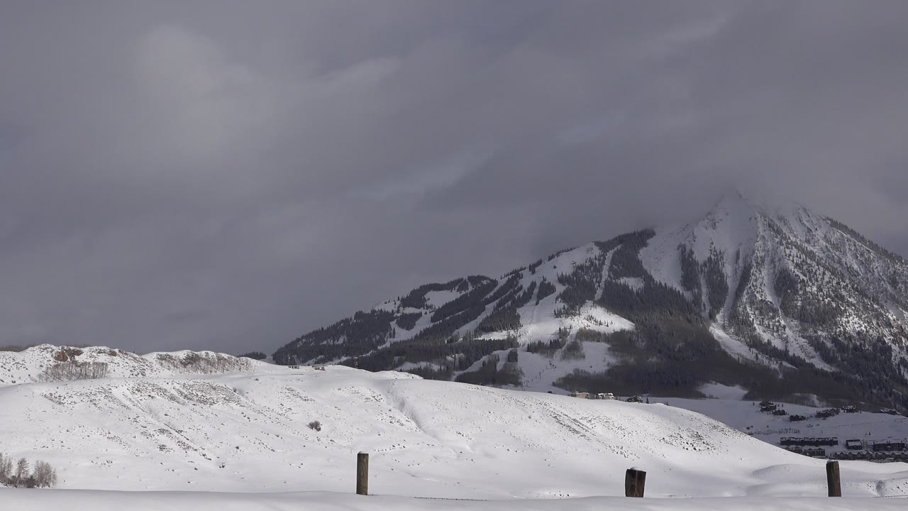 Wide winter view in Crested Butte, Colorado with snow-covered ground, scattered fence posts, a dark mountain ridge, and no visible people.