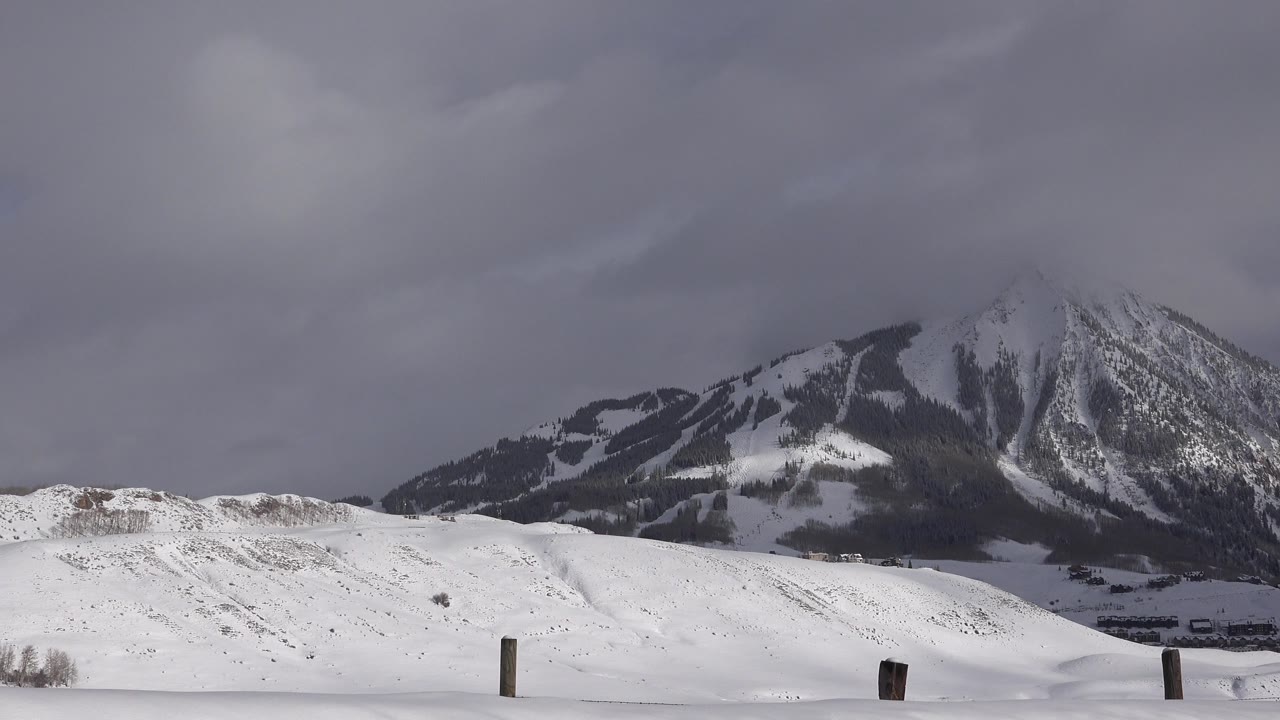 Crested Butte winter frame with bright snow in front, several fence posts, distant structures near the base of the mountain, and no visible people.