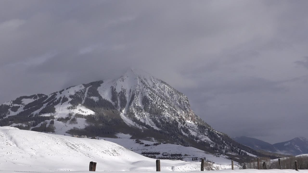 Opening frame of a snow-covered mountain in Crested Butte, Colorado with low fence posts at the bottom edge, gray cloud cover, and no visible people.