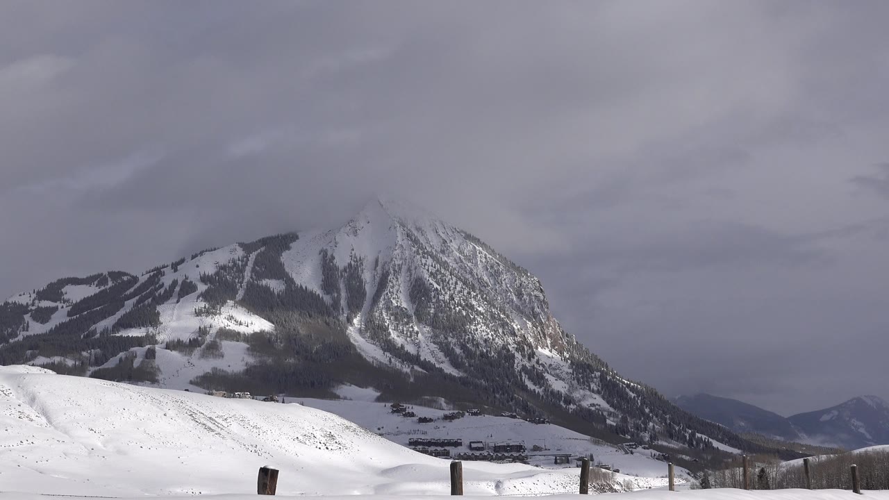 A wide winter view in Crested Butte, Colorado shows the snowy mountain ridge, open white foreground, a faint fence line, and no visible people.