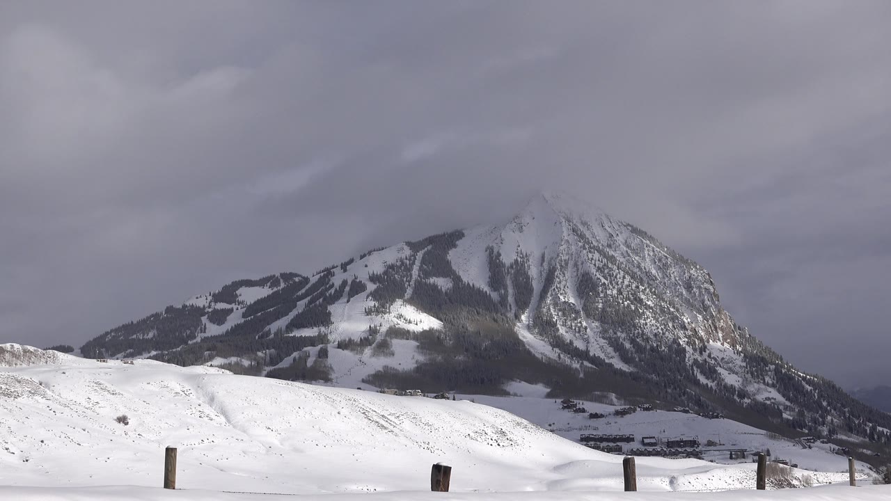 Snowy hillside and mountain beneath overcast clouds.