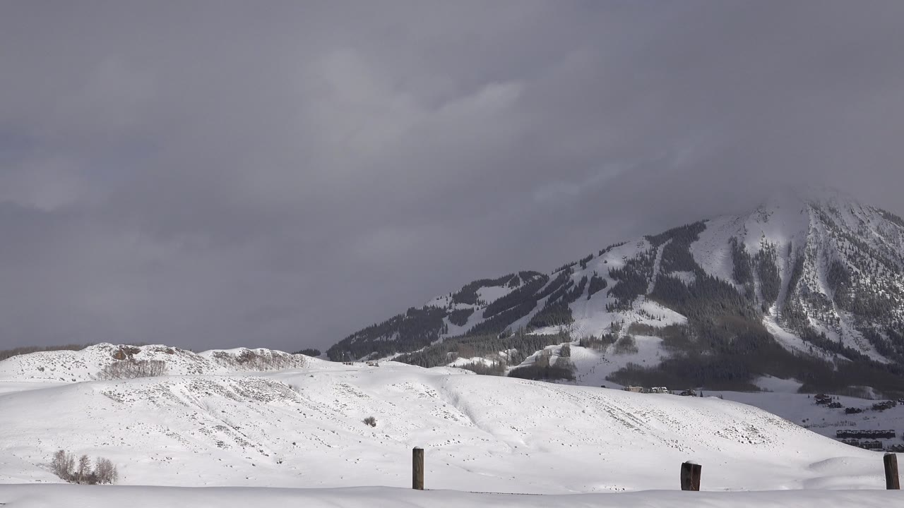 Snowy hills and mountain under thick gray cloud cover.