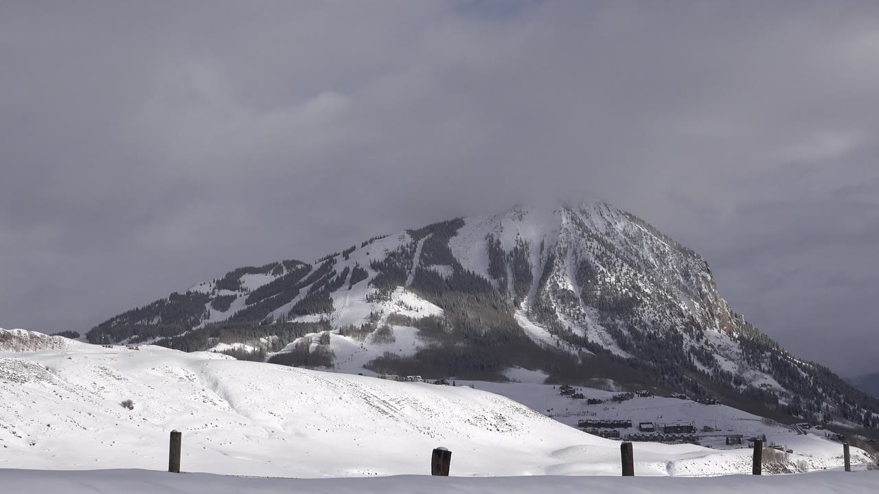 Opening frame of a snow-covered mountain near Crested Butte, Colorado, with low fence posts in the foreground and no visible people.
