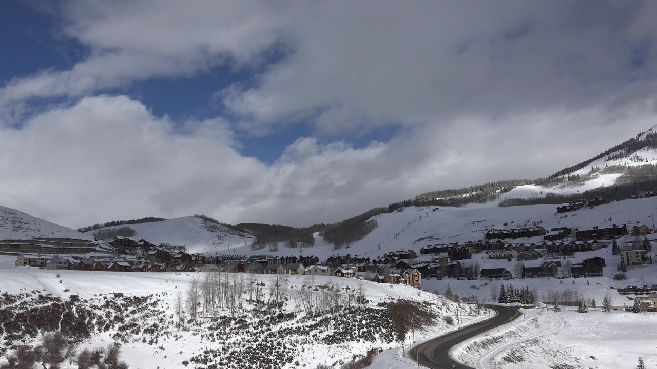Clouds over snow-covered mountain slopes and a small town area.