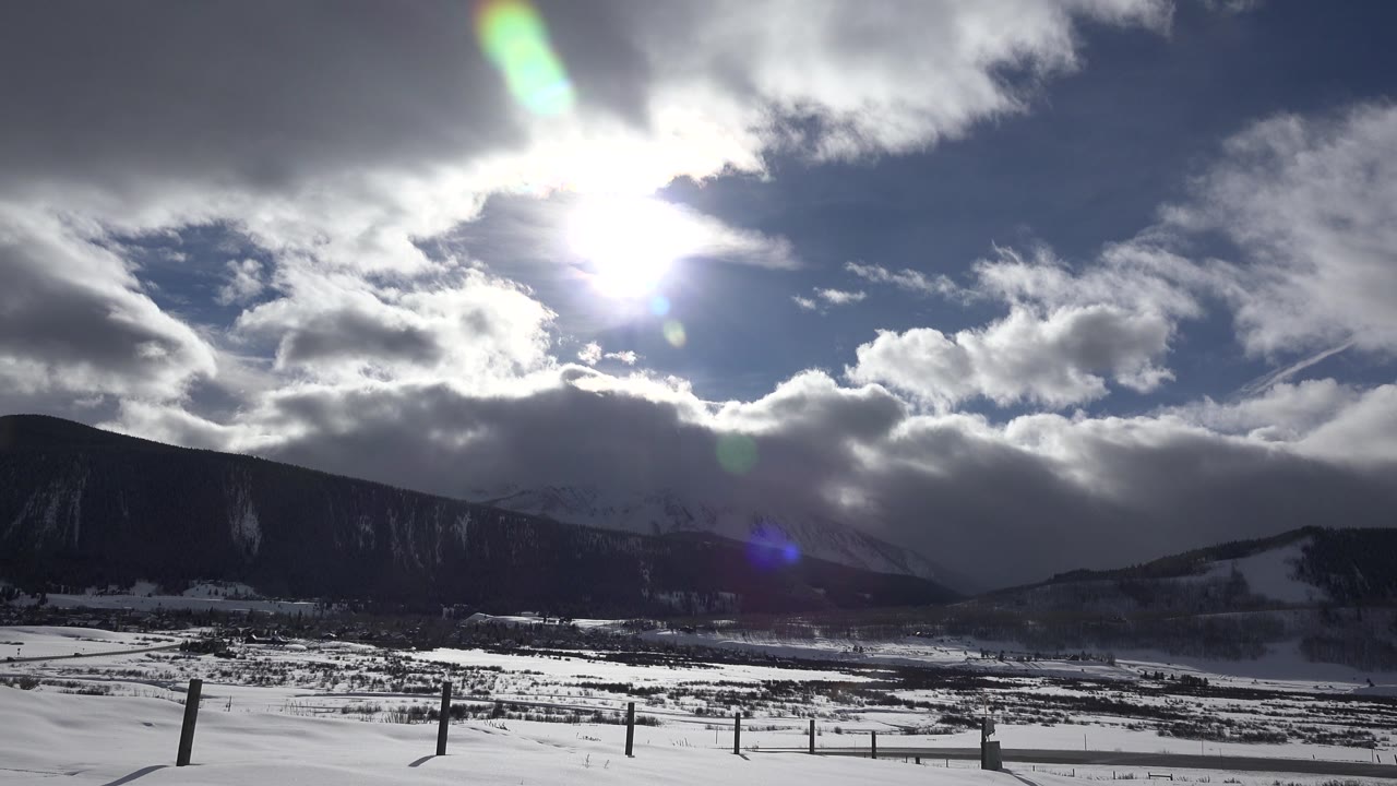 Snowy valley below bright sun and layered clouds