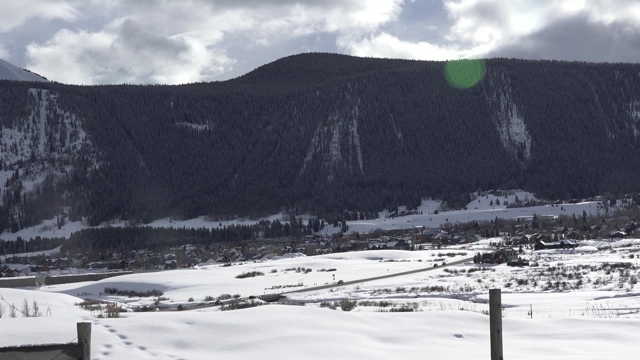 Bright snowfields and distant town below a shadowed mountain.