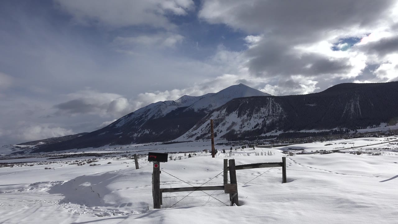 Crested Butte, Colorado winter landscape with the gate centered lower in frame, fence posts crossing the snowfield, a shadowed ridge in back, and no visible people.