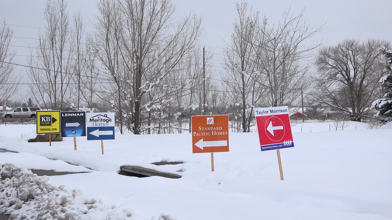 Snowy roadside with colorful home builder direction signs and bare trees