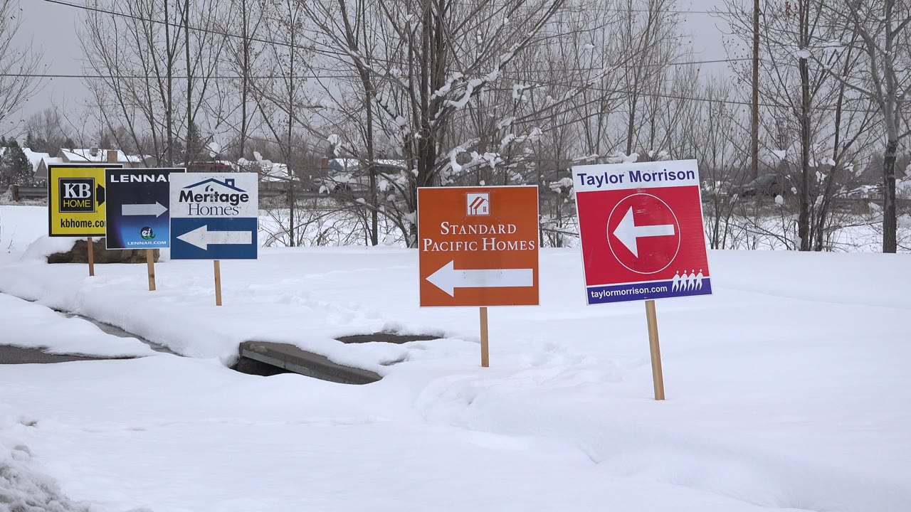 Snowy roadside with multiple homebuilder signs and bare trees.