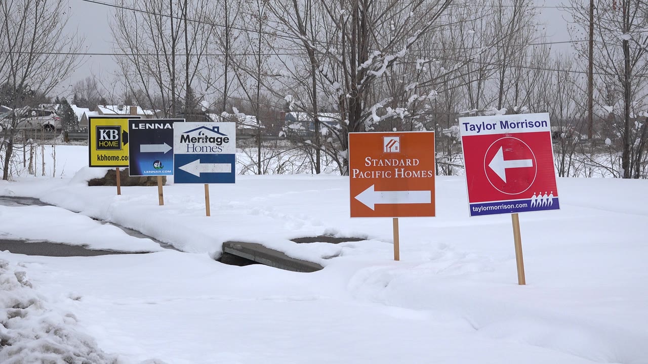 Snowy roadside with homebuilder direction signs and bare trees
