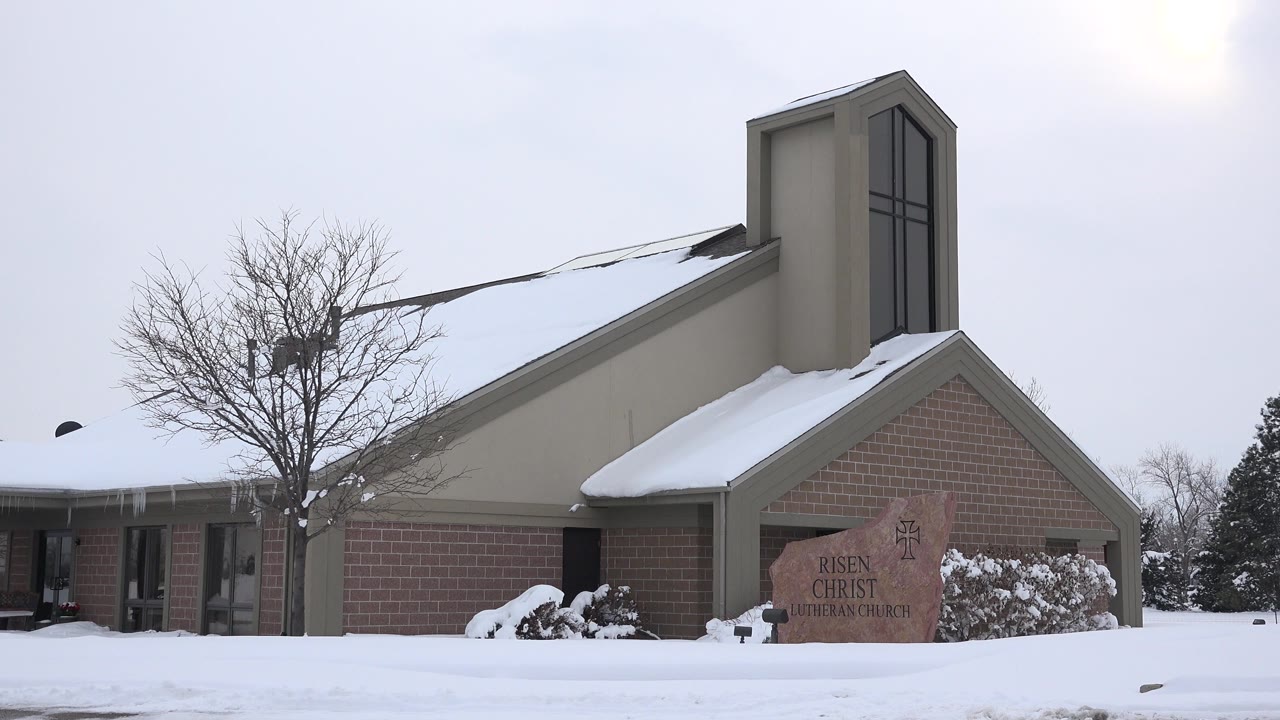 At 0:01, the Arvada, Colorado church remains framed from ground level with the leafless tree left of the roofline, snow along the lawn, and no visible people.
