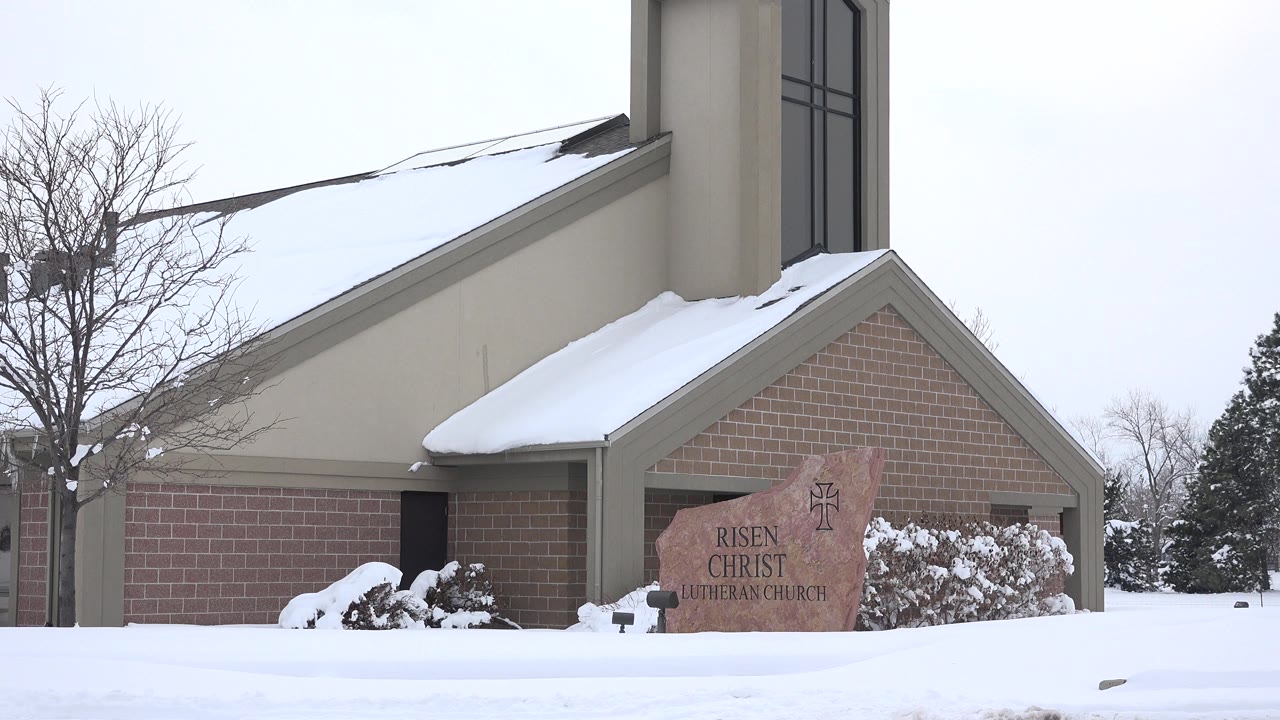 Snow-covered church exterior with brick wall and stone sign.
